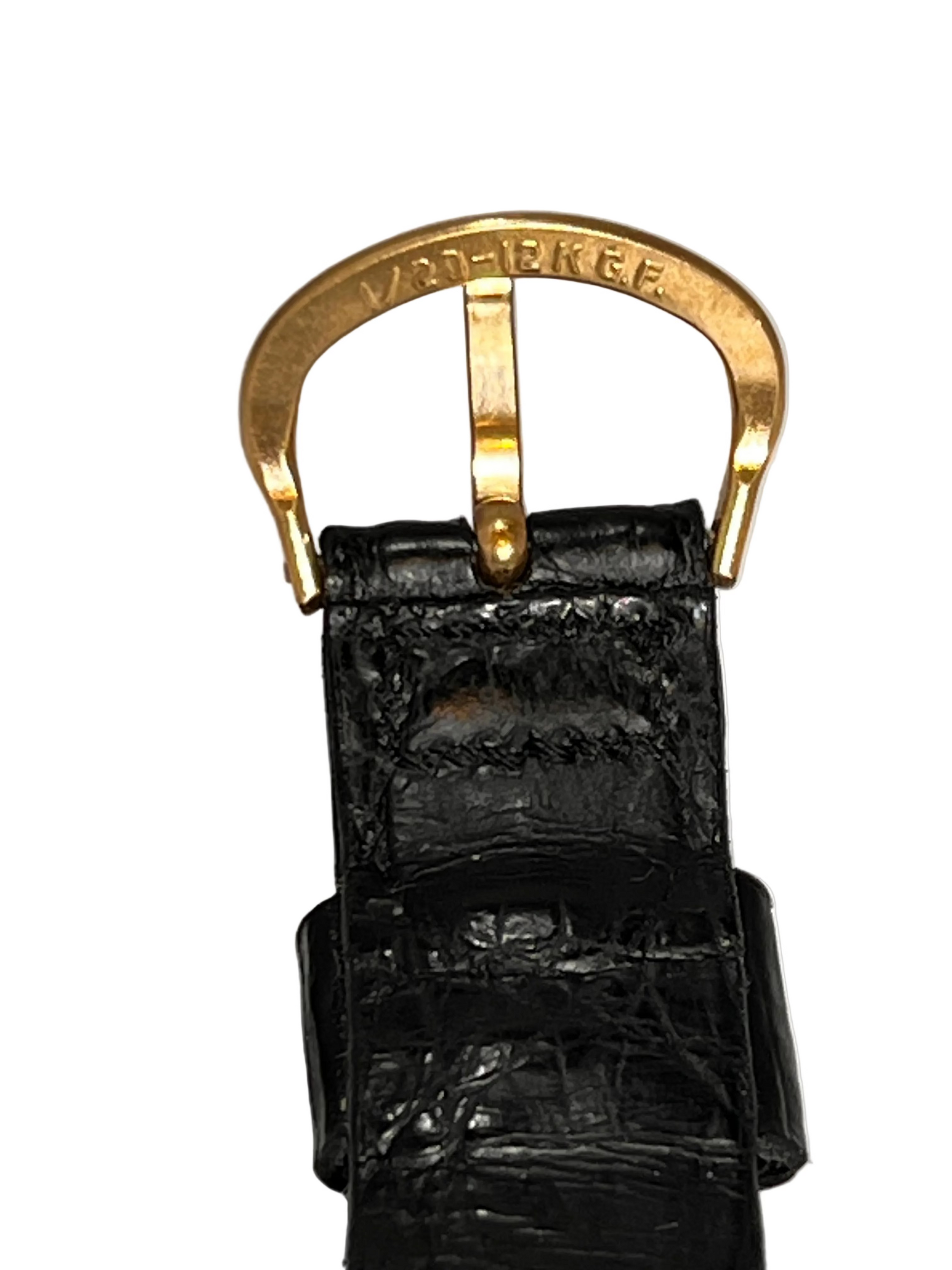 A close-up of a black crocodile-embossed leather strap with a gold-filled metal buckle 